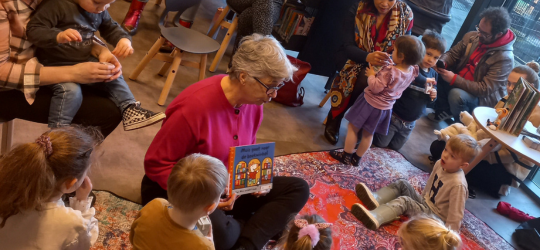 vrouw staat in de bibliotheek voor een kast met boeken met een boekstartkoffer